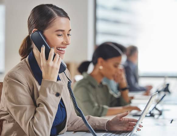 Junge Frau in Büro mit Headset telefoniert lächelnd, im Hintergrund zwei weitere Mitarbeitende an Computern, moderne Arbeitsumgebung, symbolisiert IT-Support und Kundenberatung bei dierckgroup.