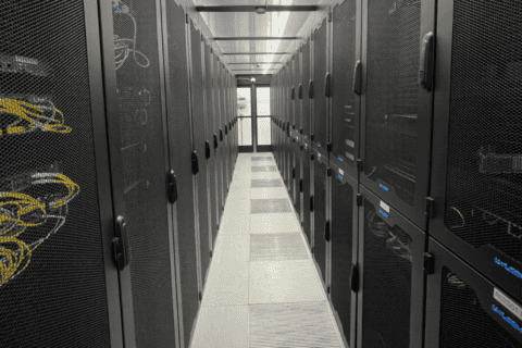 Rechenzentrum mit zwei Reihen schwarzer Serverschränke, Kabelmanagement sichtbar durch perforierte Türen, helle Deckenbeleuchtung und belüfteter Boden, symbolisiert Datacenter Solutions und IT-Infrastruktur der dierckgroup.