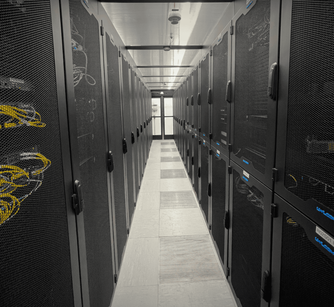 Rechenzentrum mit zwei Reihen schwarzer Serverschränke, Kabelmanagement sichtbar durch perforierte Türen, helle Deckenbeleuchtung und belüfteter Boden, symbolisiert Datacenter Solutions und IT-Infrastruktur der dierckgroup.