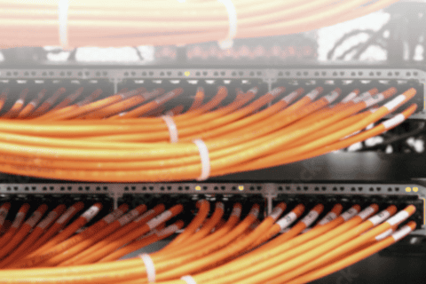 Mehrere Reihen von orangefarbenen Netzwerkkabeln, ordentlich gebündelt und in Patchpanel-Steckplätze eingesteckt, Teil einer IT-Infrastruktur für Netzwerklösungen und IT-Security in einem Rechenzentrum.