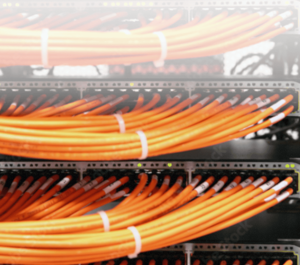Mehrere Reihen von orangefarbenen Netzwerkkabeln, ordentlich gebündelt und in Patchpanel-Steckplätze eingesteckt, Teil einer IT-Infrastruktur für Netzwerklösungen und IT-Security in einem Rechenzentrum.