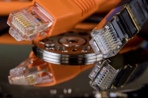 Nahaufnahme von zwei Ethernet-Kabeln, eines orange und eines schwarz, die an eine geöffnete Festplatte angeschlossen sind, symbolisieren digitale Datensicherung und Netzwerklösungen.