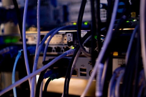 Verschiedene Netzwerkkabel in einem Server-Rack, verbunden mit einem Patchpanel und Netzwerkgeräten, beleuchtet in einem Rechenzentrum, symbolisiert IT-Infrastruktur und Cloud-Services.