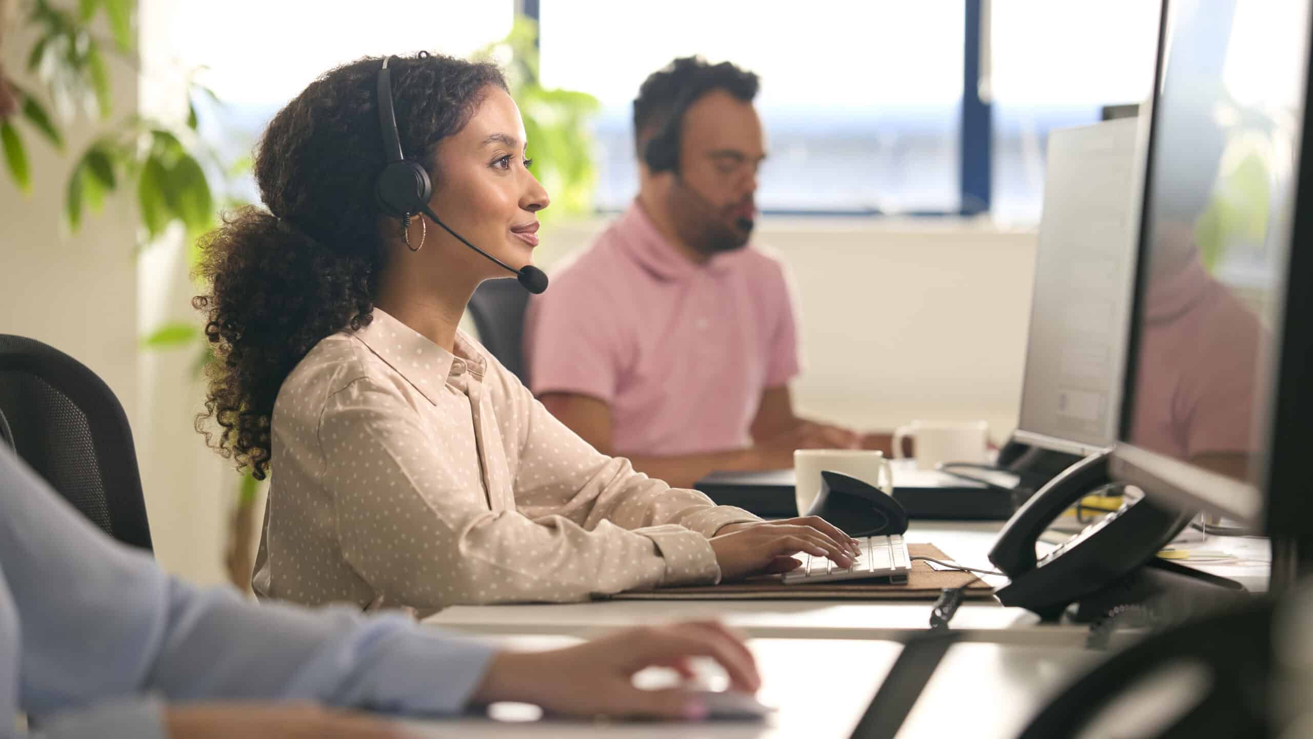 Mehrere Mitarbeitende in einem modernen Büro mit Headsets arbeiten konzentriert an Computern, symbolisieren IT-Support und Kommunikationstechnik in einem professionellen Umfeld.