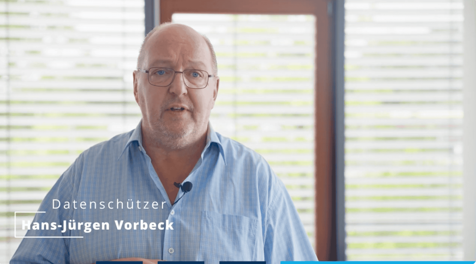 Mann mittleren Alters mit Brille und blauem Hemd vor Fenster mit Jalousien, eingeblendeter Text „Datenschützer Hans-Jürgen Vorbeck“, spricht in ein Mikrofon am Hemdkragen.