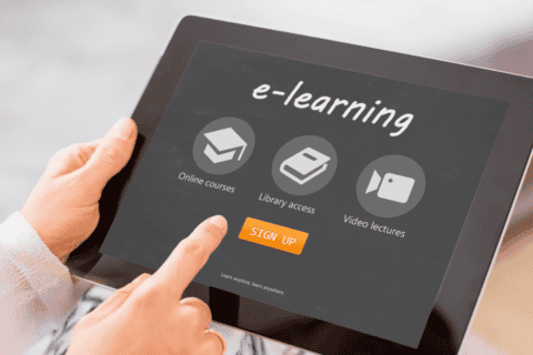 Tablet mit e-learning Startseite, darauf Symbole für Online-Kurse, Bibliothekszugang und Video-Vorlesungen, darunter ein orangefarbener Button mit der Aufschrift „Sign Up“, gehalten von einer Person mit hellem Pullover, die mit dem Finger auf den Bildschirm zeigt.