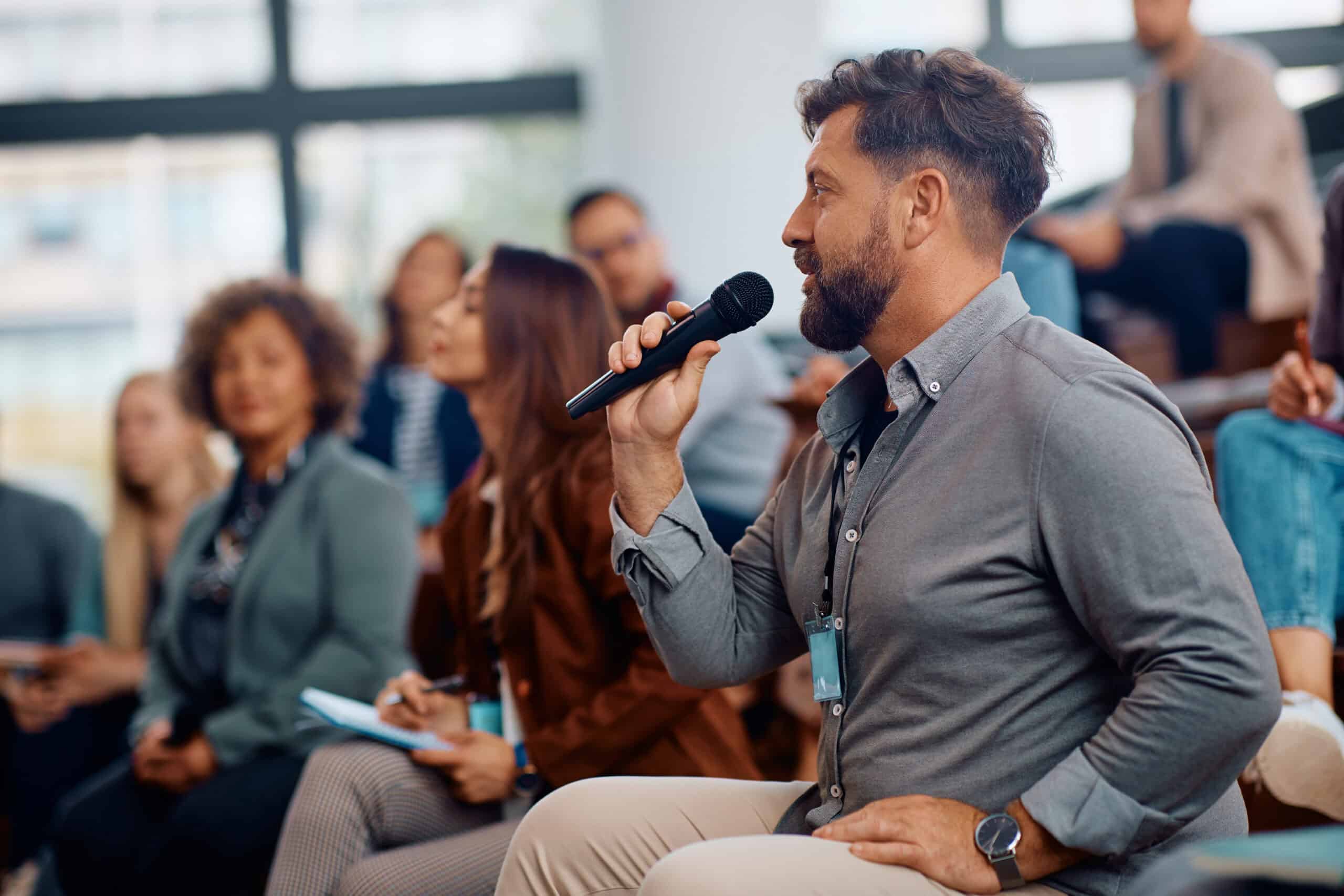 Mann mit Mikrofon stellt Frage bei Business-Seminar, umgeben von weiteren Teilnehmern in moderner Konferenzhalle, symbolisiert IT-Beratung und Kommunikationstechnik bei dierckgroup.
