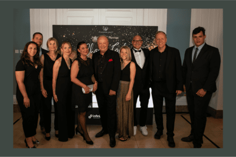 Zehn Personen in eleganter Abendkleidung stehen vor einer Fotowand mit goldenen Sternen und dem Schriftzug „Infinity Nuvias Charity Gala“. Die Gruppe lächelt in die Kamera, im Hintergrund sind Logos von Infinity und Nuvias zu sehen. Die Szene vermittelt einen festlichen Anlass, passend zu professionellen Netzwerken und Events.
