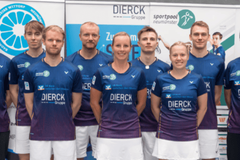 Acht Personen in einheitlichen Sporttrikots mit dem Schriftzug „dierckgroup“ stehen nebeneinander vor Werbebannern, die unter anderem die dierckgroup, Sportpool Neumünster und VR Bank Neumünster zeigen. Die Trikots sind dunkelblau mit lila Akzenten, die Personen wirken als Team, passend zum Kontext von IT Solutions und Managed Services der dierckgroup.