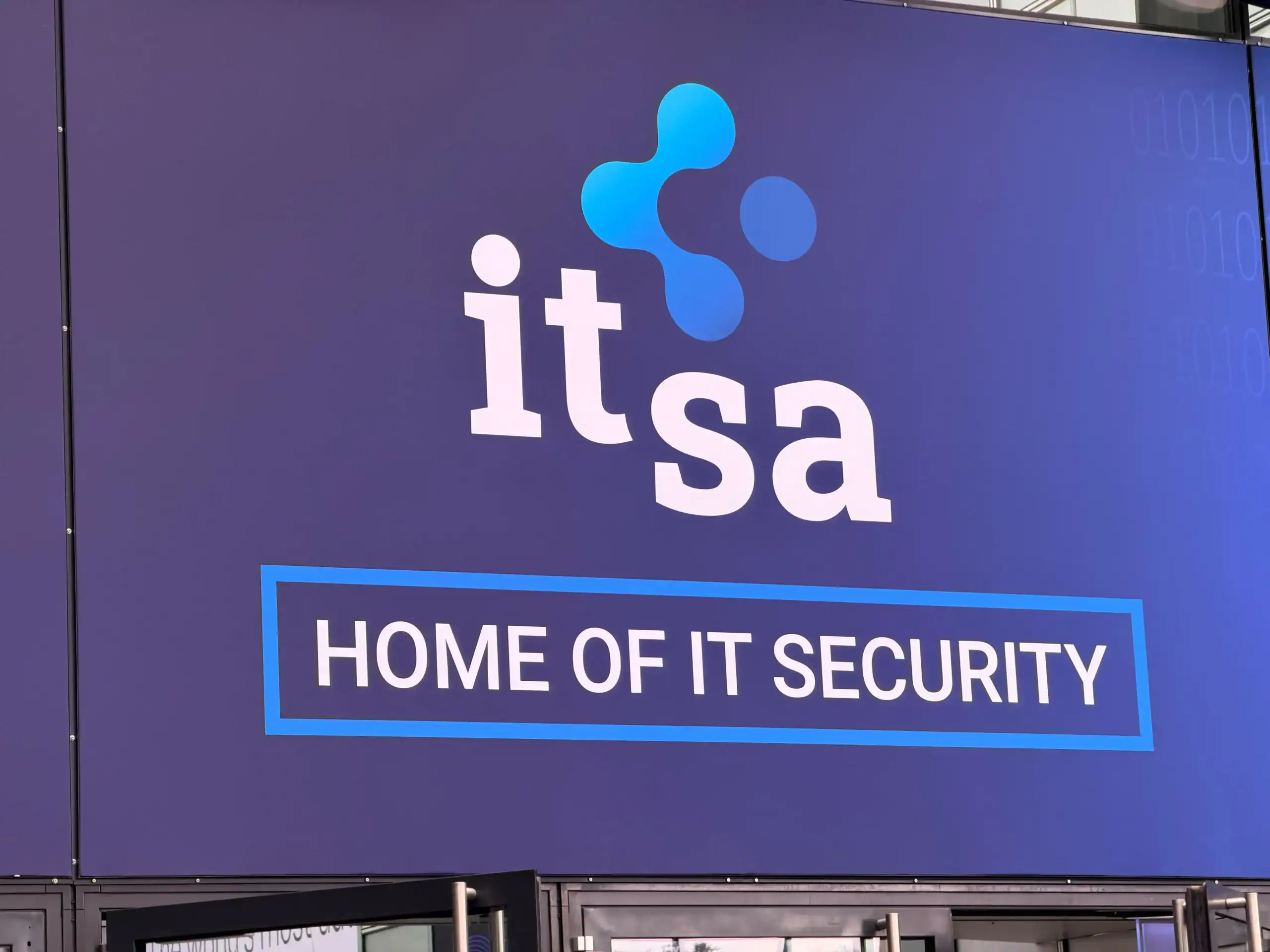 Logo der it-sa auf blauem Hintergrund mit dem Schriftzug „HOME OF IT SECURITY“ in einem blauen Rahmen, Hinweis auf IT-Security und Digitalisierung.